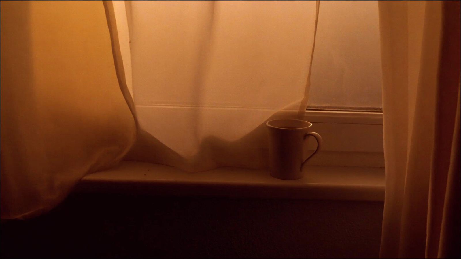 Una ventana al amanecer con luz cálida y una taza sola en el alféizar.