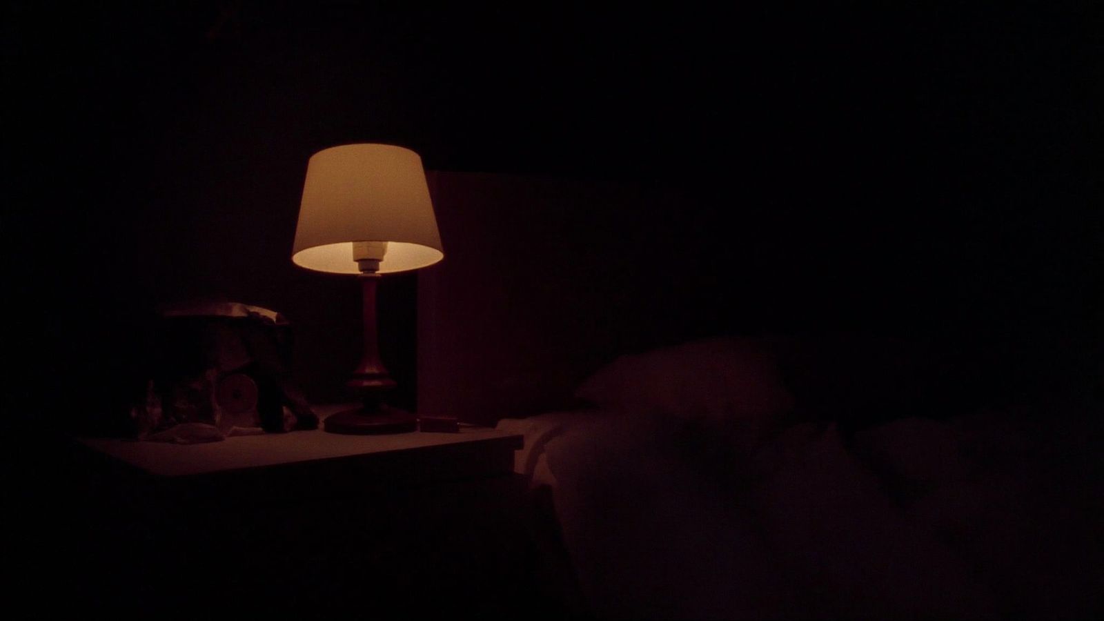 Una lámpara encendida junto a una cama a oscuras, de madrugada.