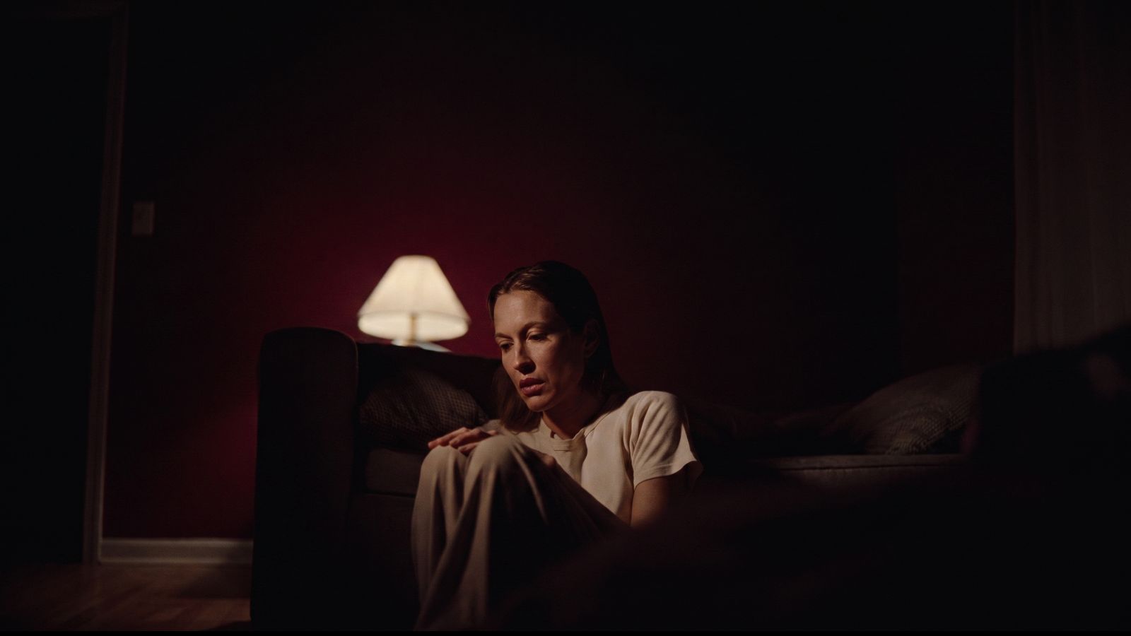 Una mujer sentada en el suelo de su dormitorio, de madrugada, a la luz cálida de una lámpara.