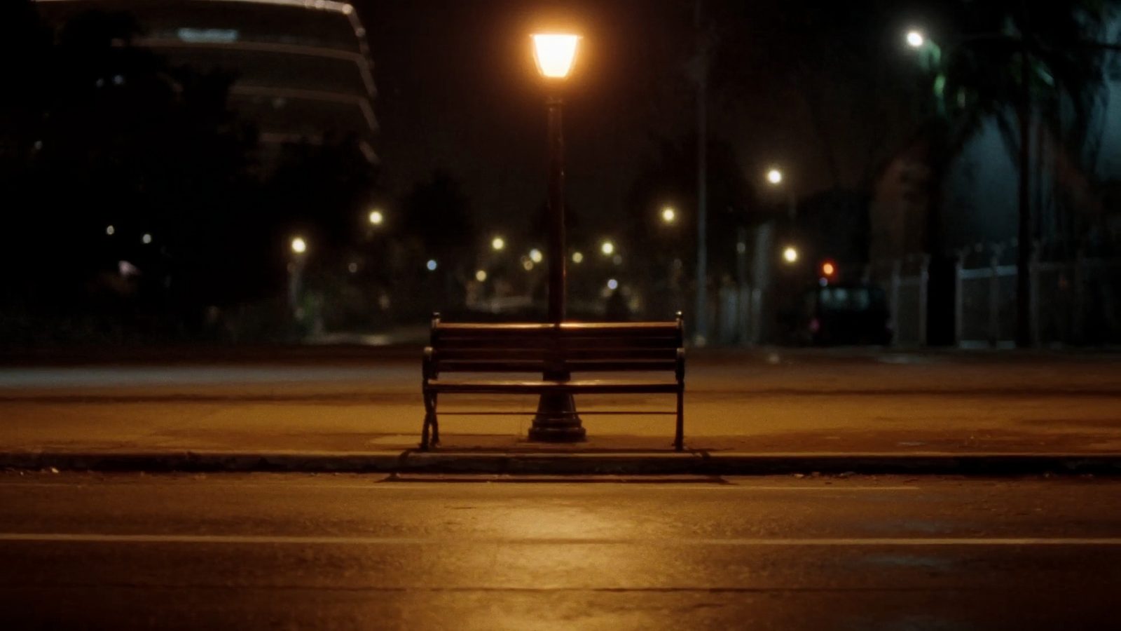 Un banco vacío bajo una farola, de noche, con la ciudad desenfocada detrás.