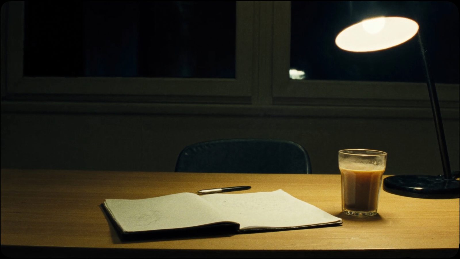 Un escritorio de noche con un cuaderno abierto en blanco y una silla vacía.